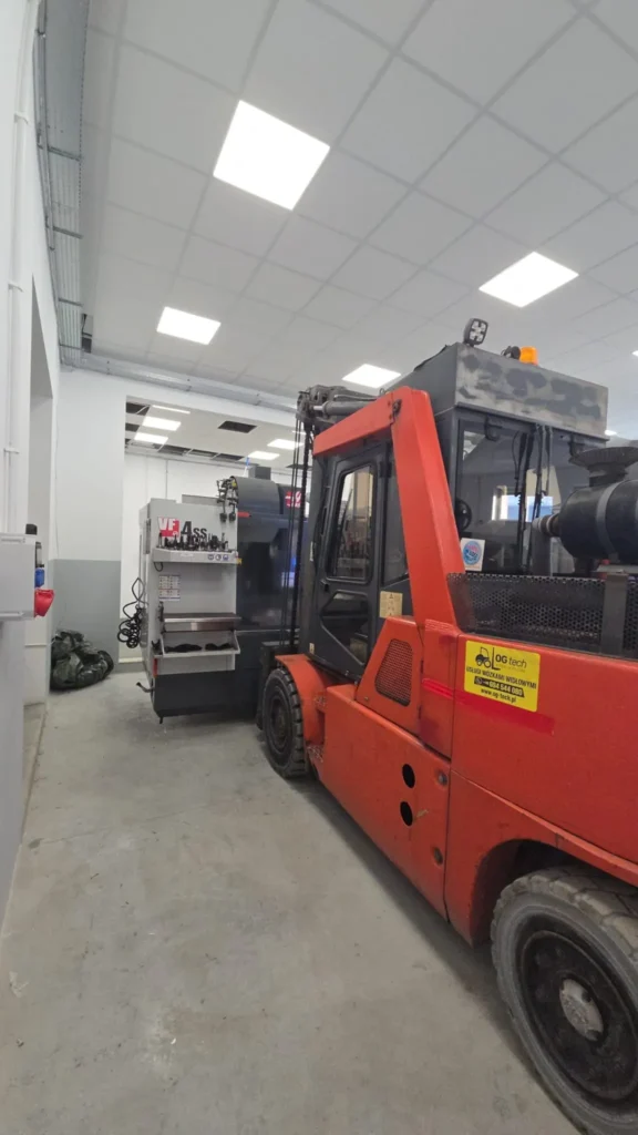 Transport maszyny CNC Haas VF-4SS wózkiem widłowym podczas relokacji w hali przemysłowej